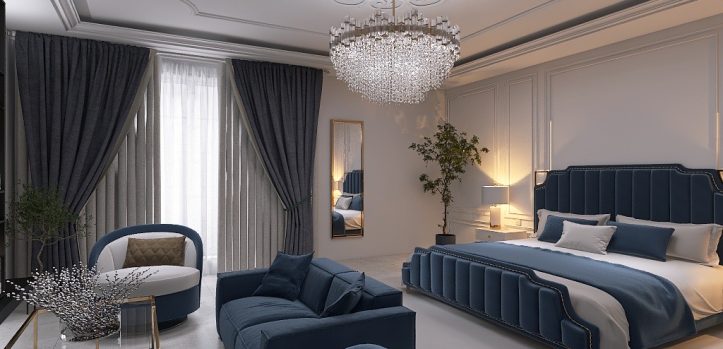 Elegante camera da letto con un grande letto imbottito blu navy. Un divano coordinato e una sedia circolare sono di fronte a un tavolino da caffè in vetro. Un lampadario di cristallo pende dal soffitto. Alte tende blu navy fiancheggiano una finestra e un grande specchio è accanto a una pianta in vaso.