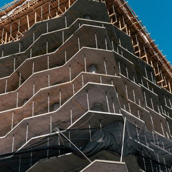 Il cantiere di Cila ROma presenta un edificio a più piani con balconi angolari e sporgenti e reti di sicurezza. Le impalcature sono visibili ai piani superiori contro un cielo azzurro terso, a testimonianza dell'impegno di Cila ROma per l'innovazione architettonica moderna.